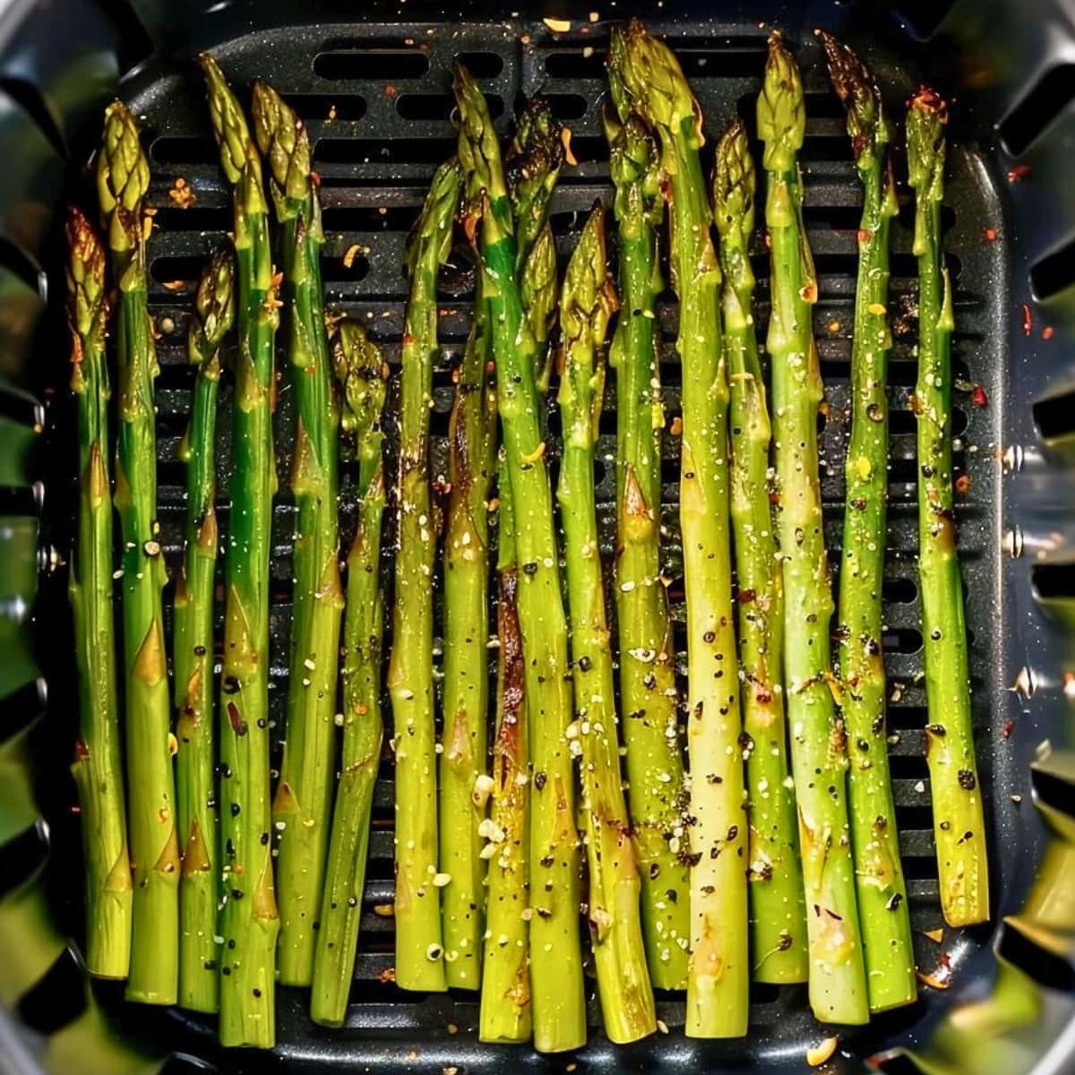 Seasoned asparagus arranged inside an air fryer basket.