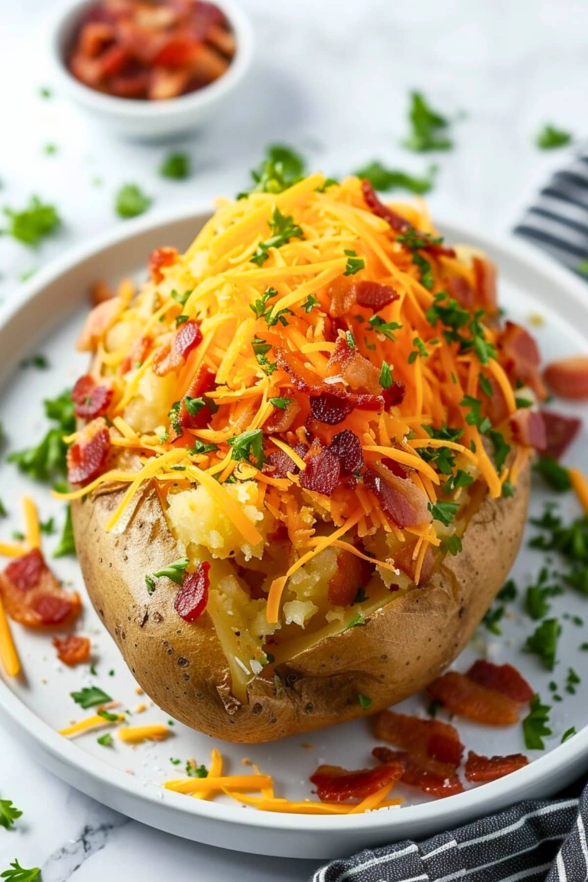 Baked potato on a plate topped with shredded cheese and bacon bits.