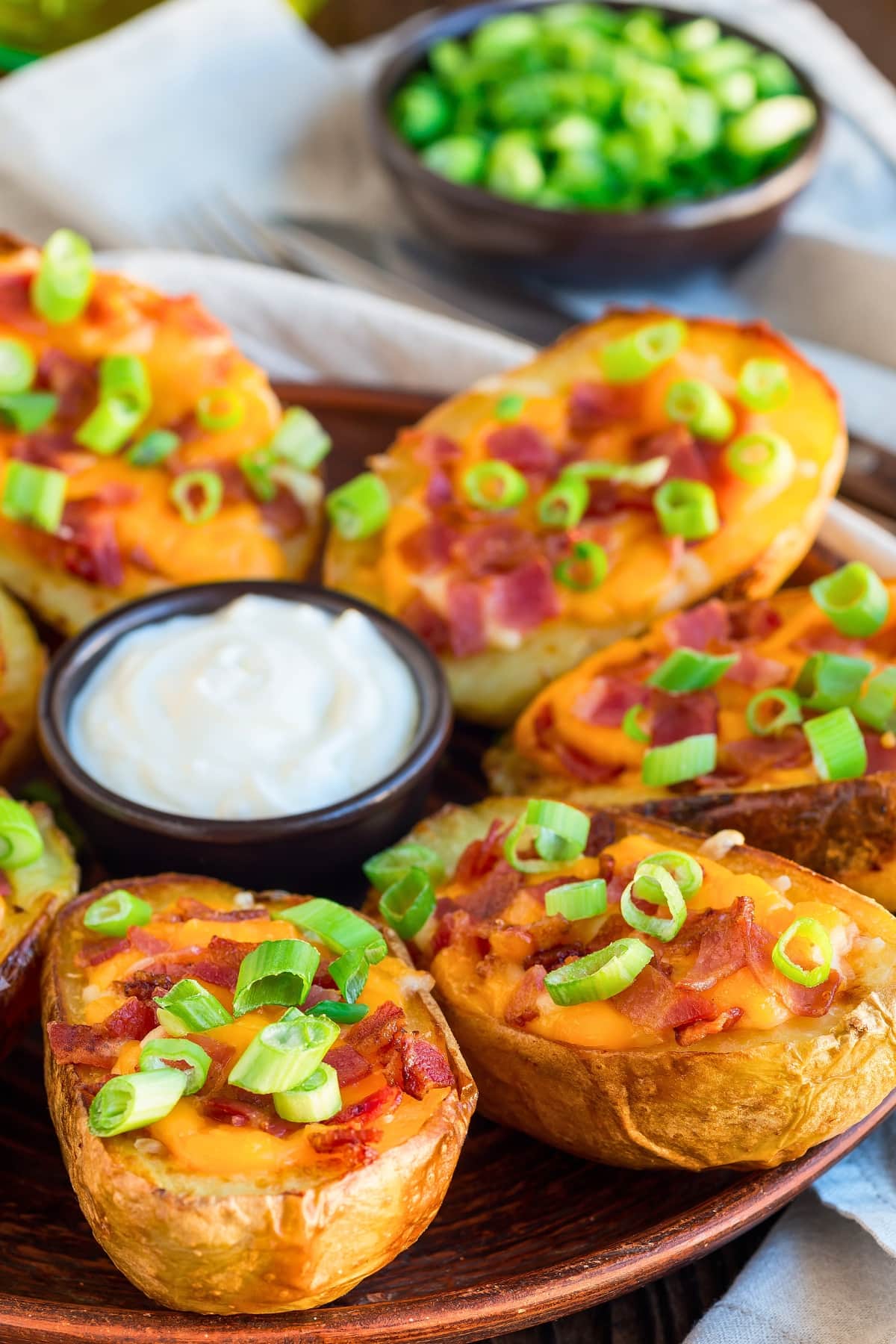 Potato skins arranged in a wooden tray with cheesy filling garnished with chopped bacon.