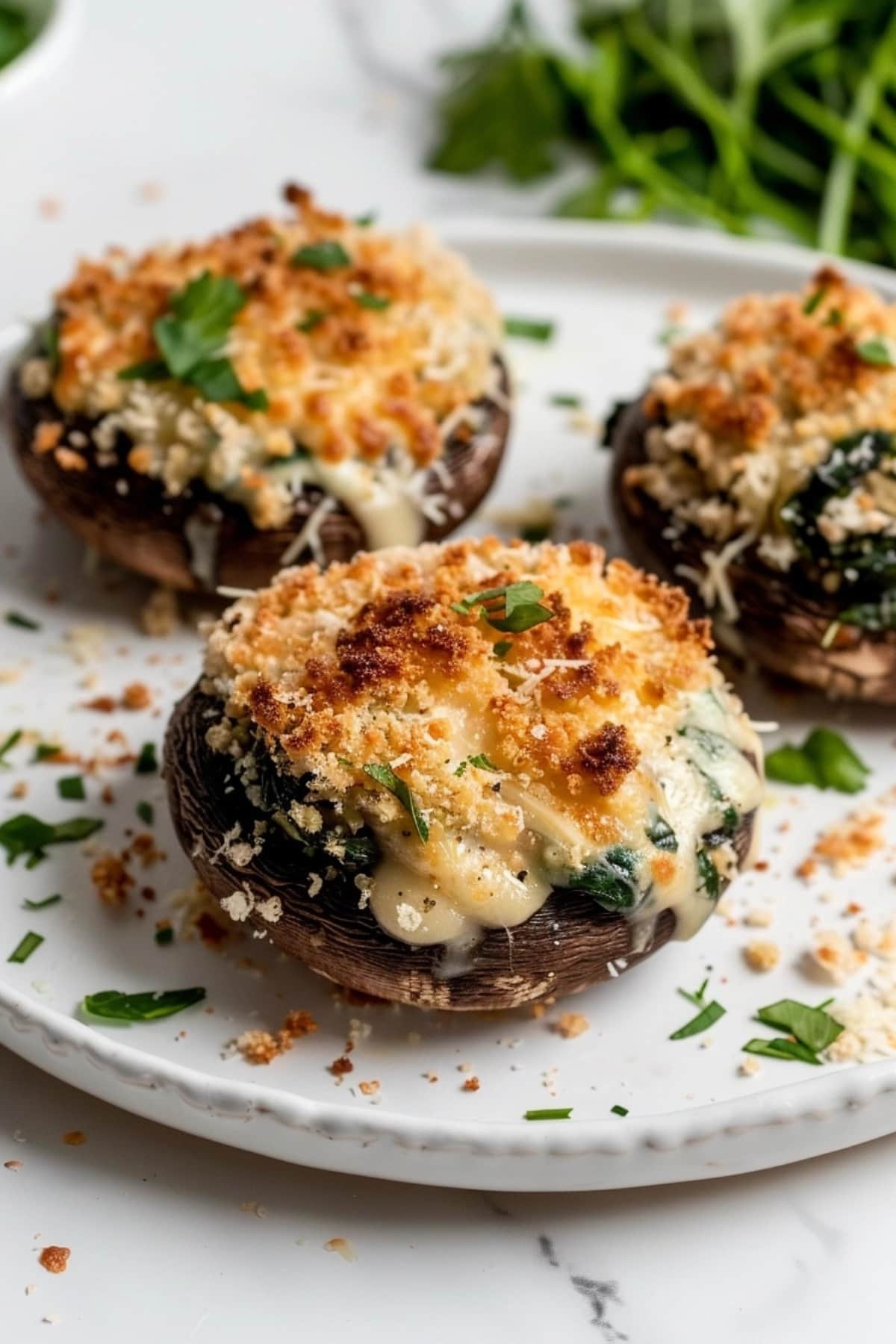 Baked Stuffed Portobello Mushrooms served on a white plate topped with cheese and breadcrumbs garnished with chopped parsley leaves.