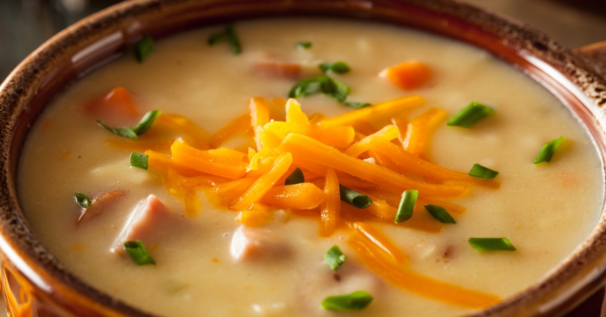 Beer cheese soup in a pot garnished with shaved cheese.