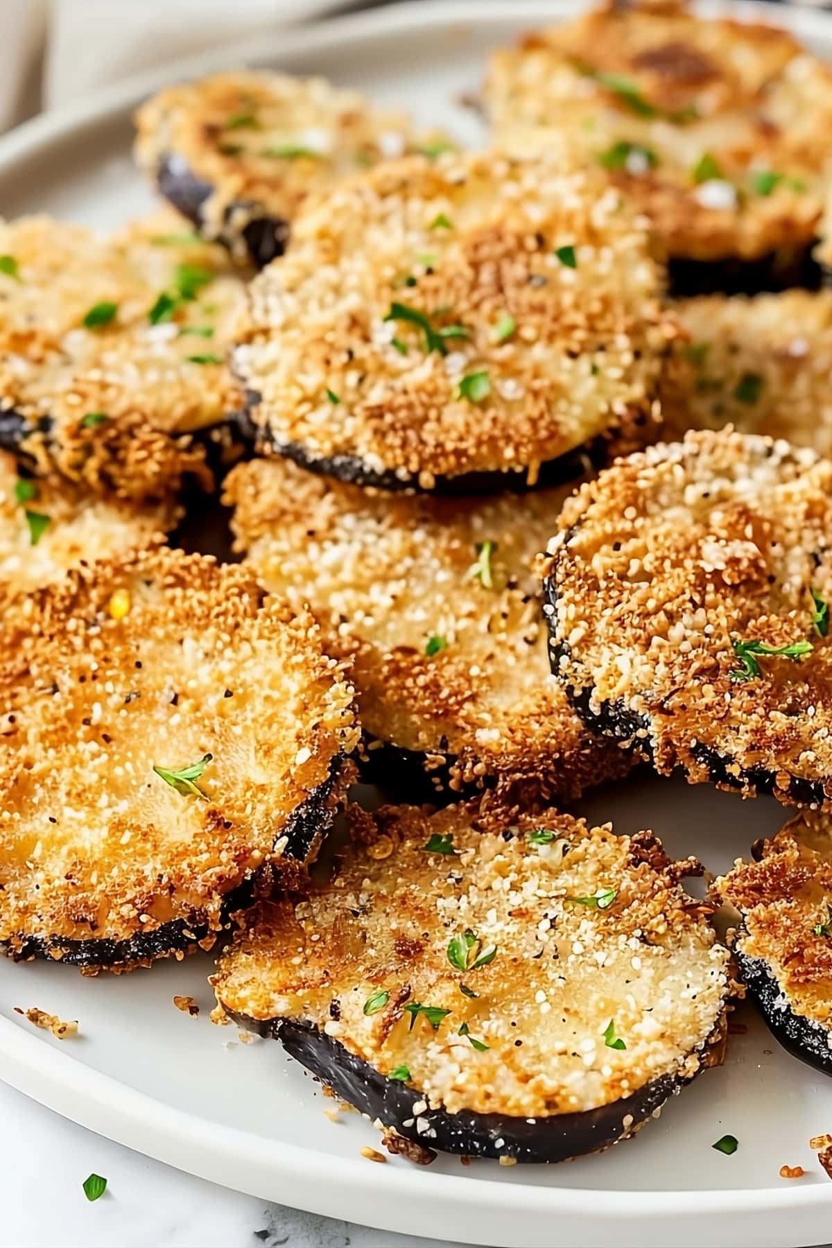 Round sliced eggplant breaded in a white plate.