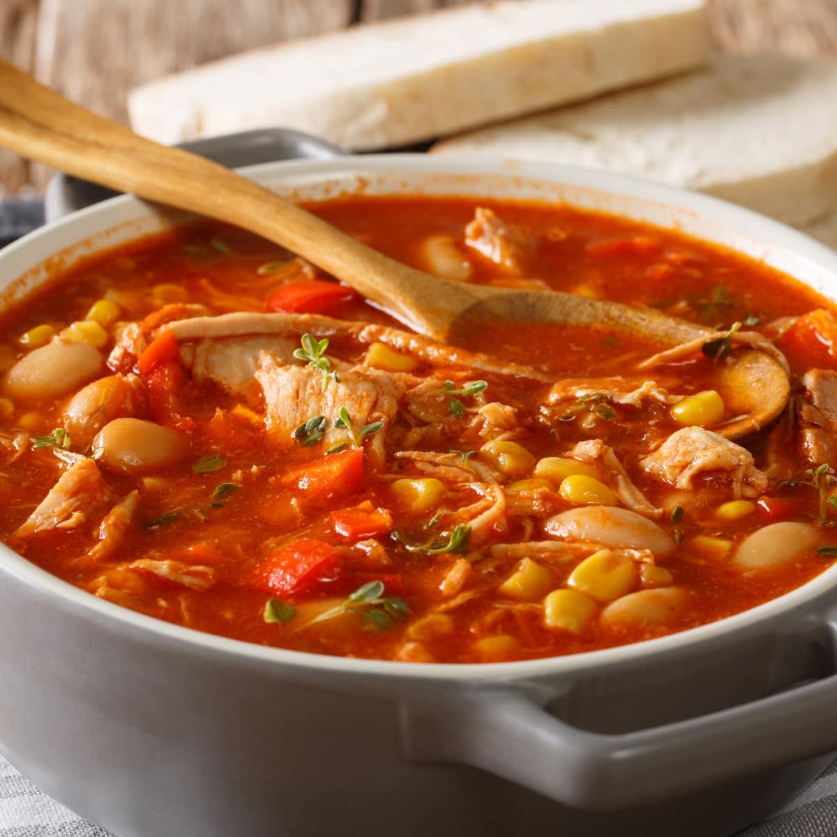 A wooden ladle dipped in a pot of Brunswick stew made with tomato base, chicken, veggies and beans.
