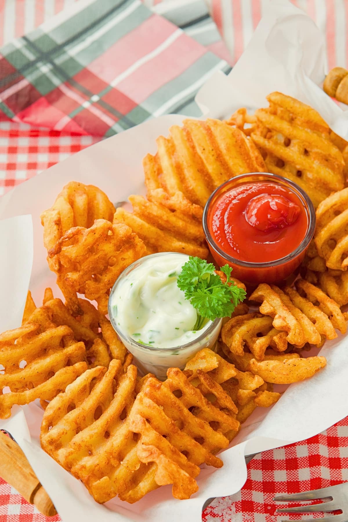 Bunch of air fries waffle fries in a basket with lining served with ketchup and mayo dip.