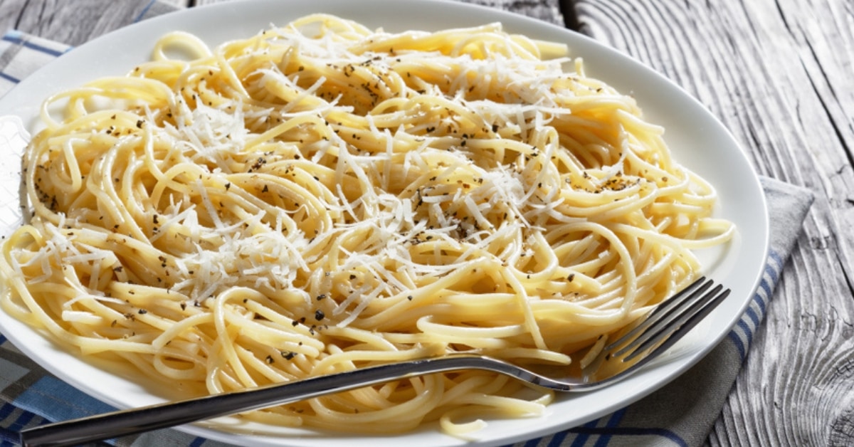 Cacio E pepe pasta cooked in a white plate with grated cheese and black pepper on a concrete table.