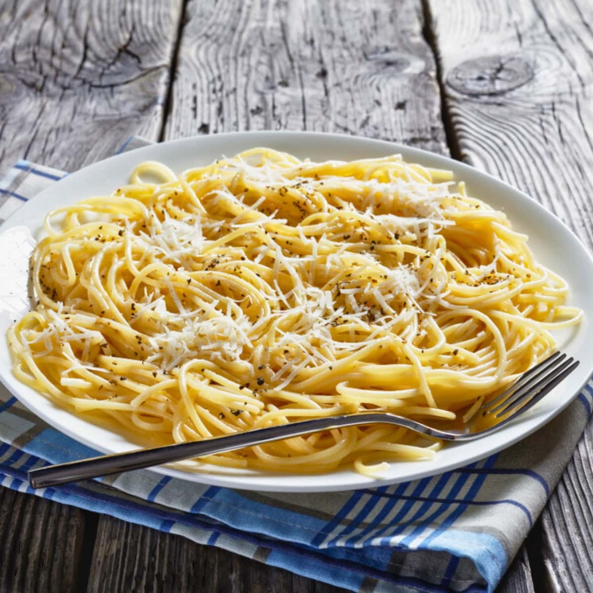 Serving of Cacio E Pepe on a plate with grated cheese garnish and black pepper.