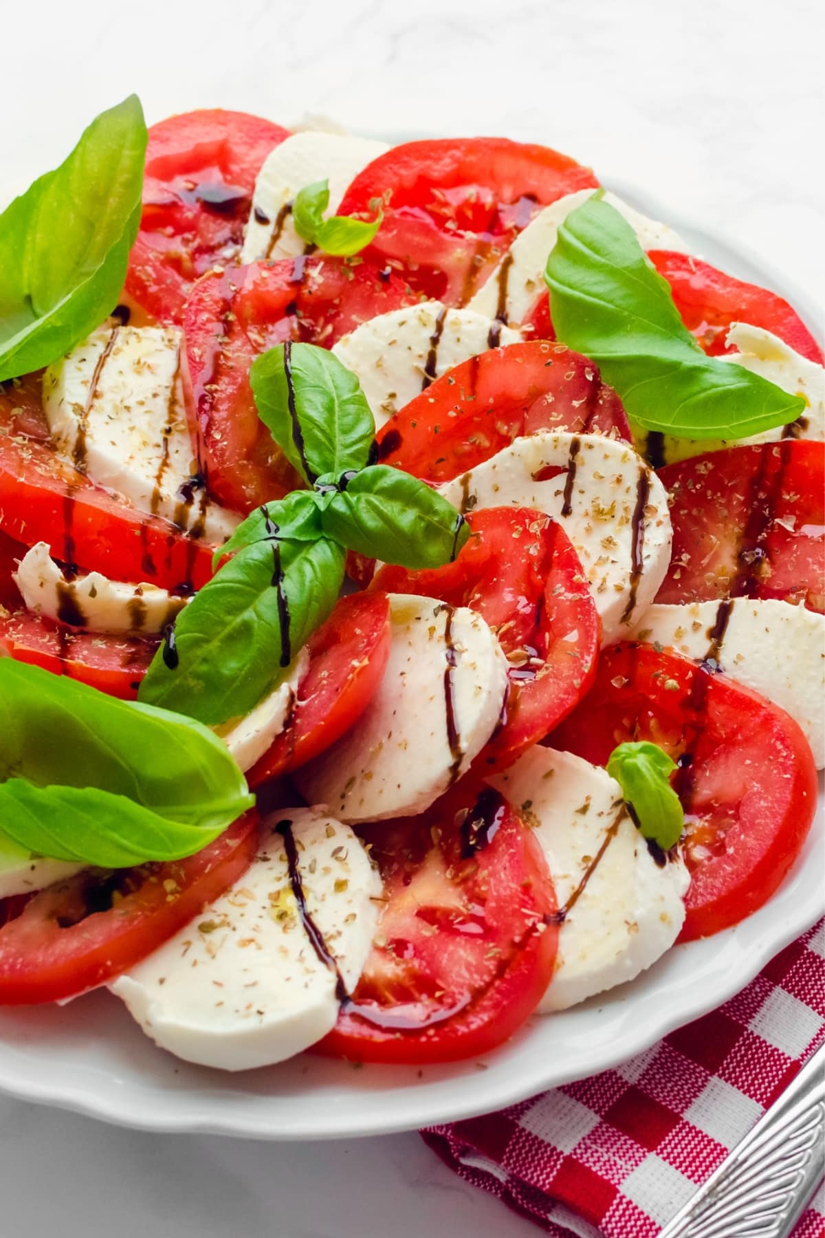 Caprese salad made with sliced tomatoes. mozzarella cheese and basil leaves drizzled with balsamic dressing and olive oil.