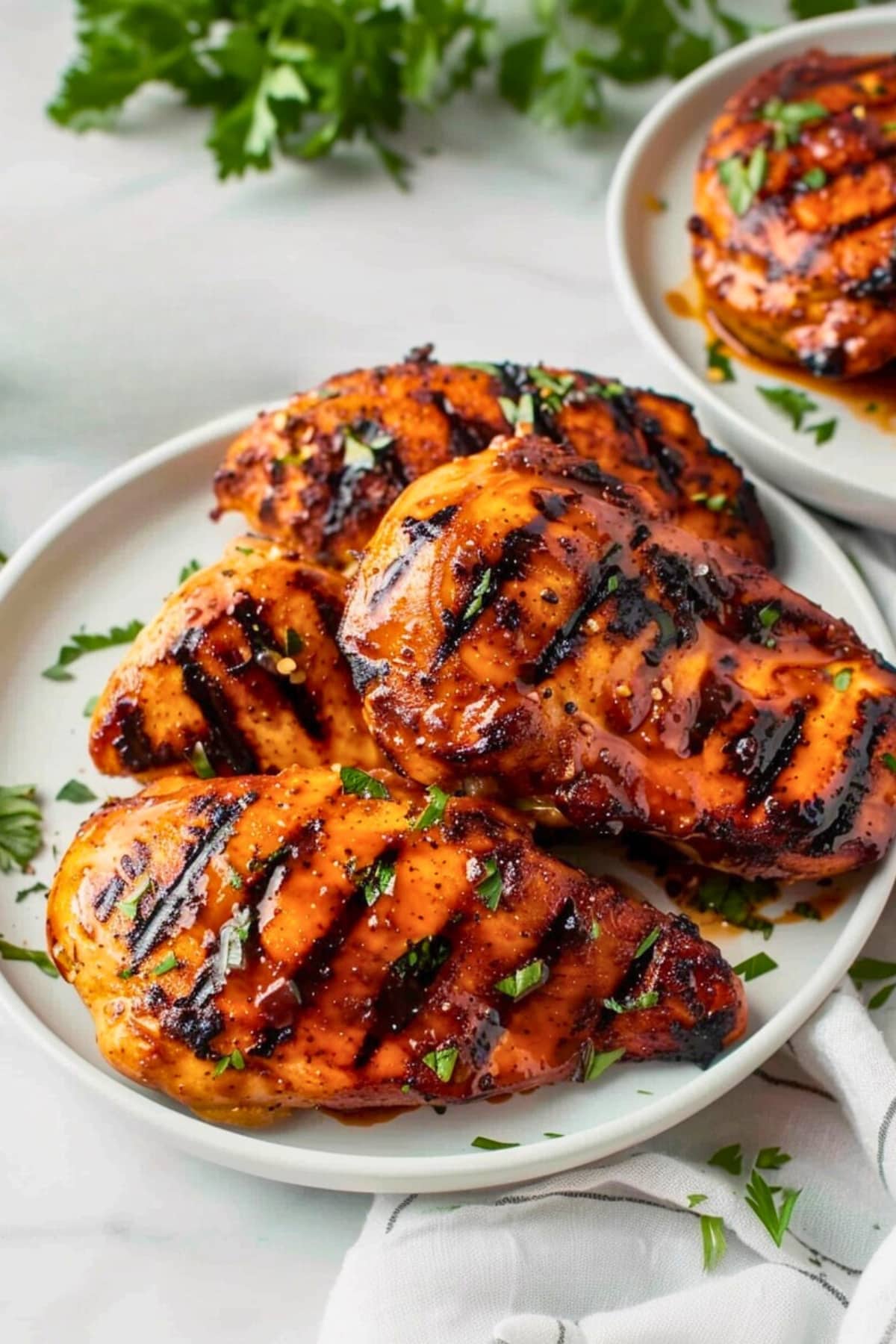 Grilled chicken breast brushed with barbecue sauce served on a white plate.