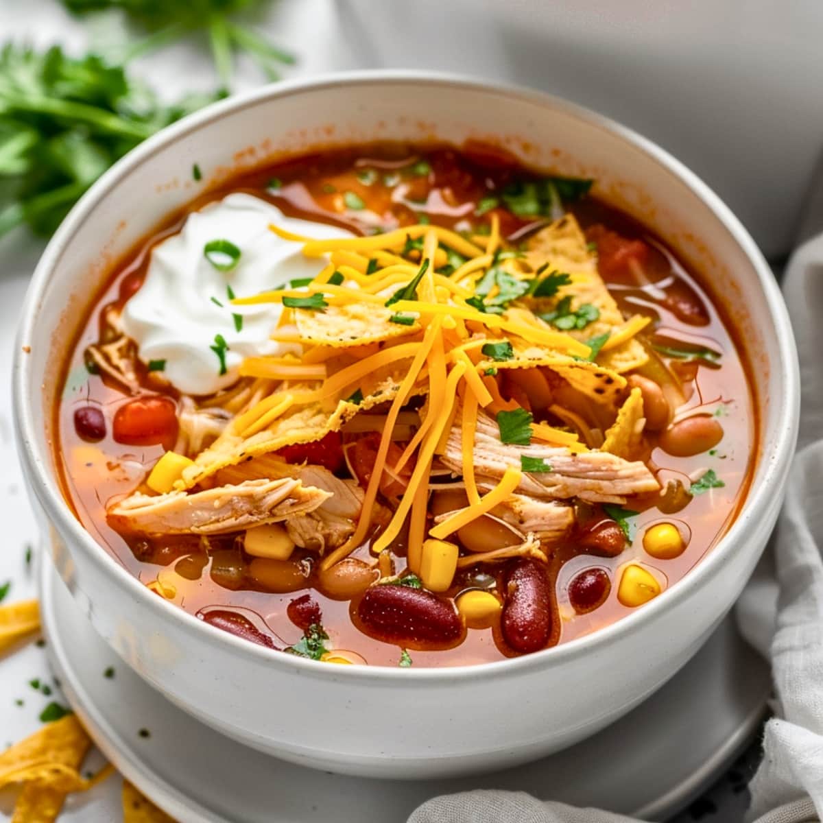 White bowl with chicken tortilla soup topped with shredded cheddar cheese.