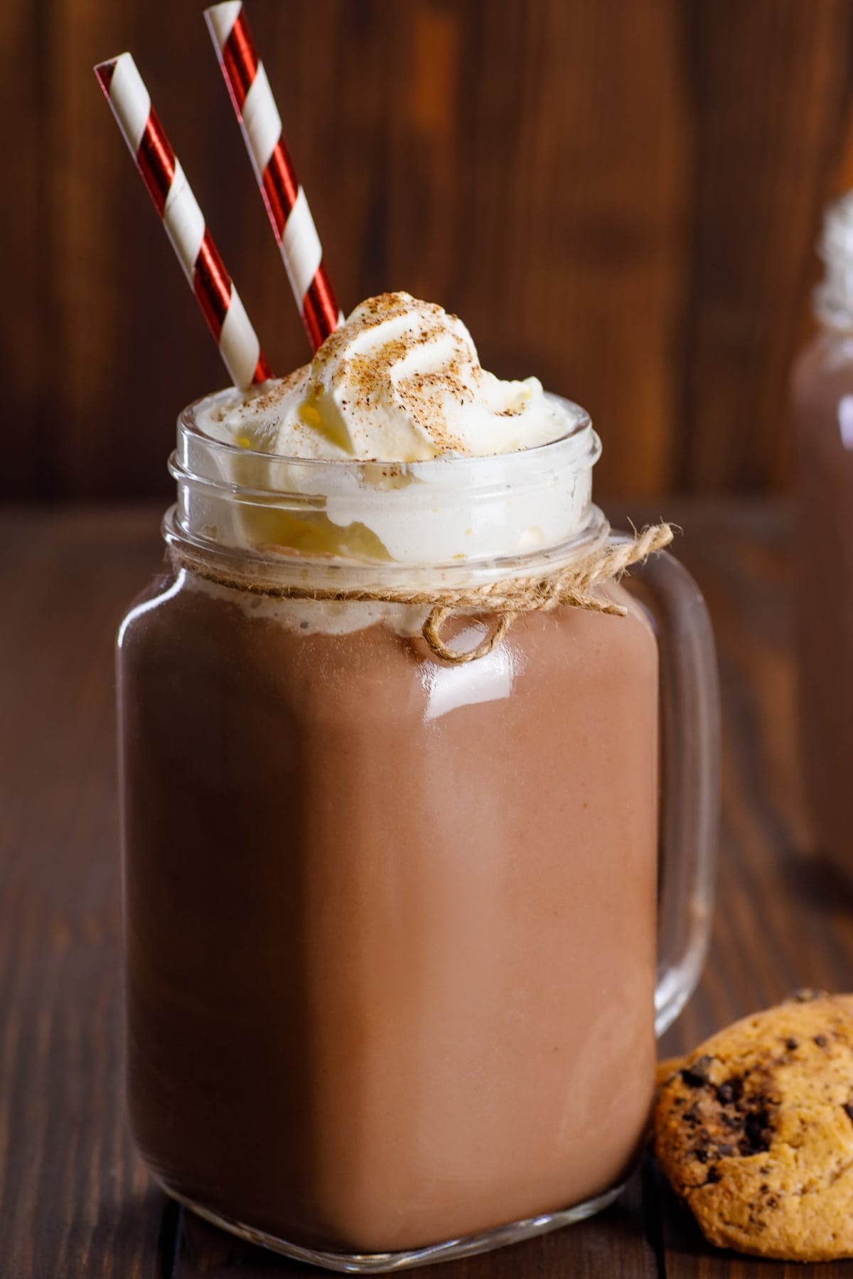Chocolate milkshake in a glass mug topped with whipped cream and straw.