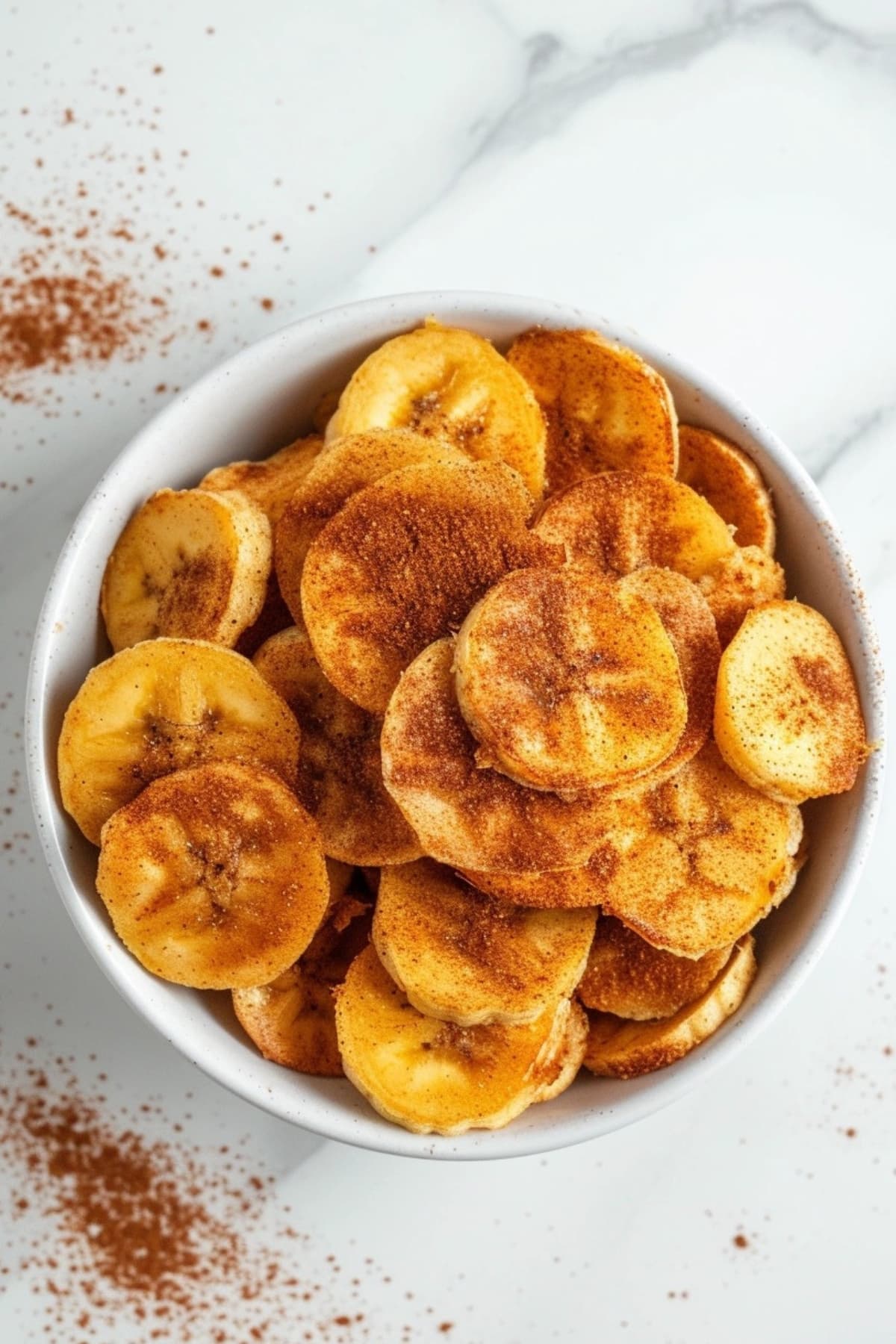 Banana chips in a white bowl sprinkled with cinnamon powder.