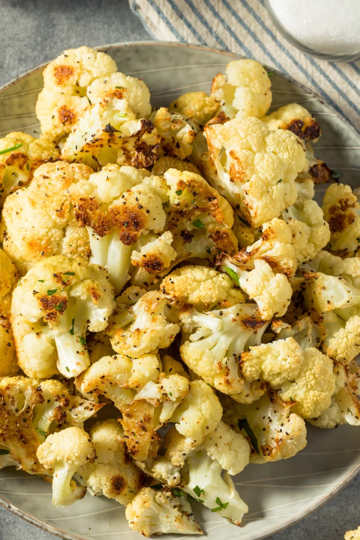 Bunch of roasted cauliflower in a plate sprinkled with chopped parsley.
