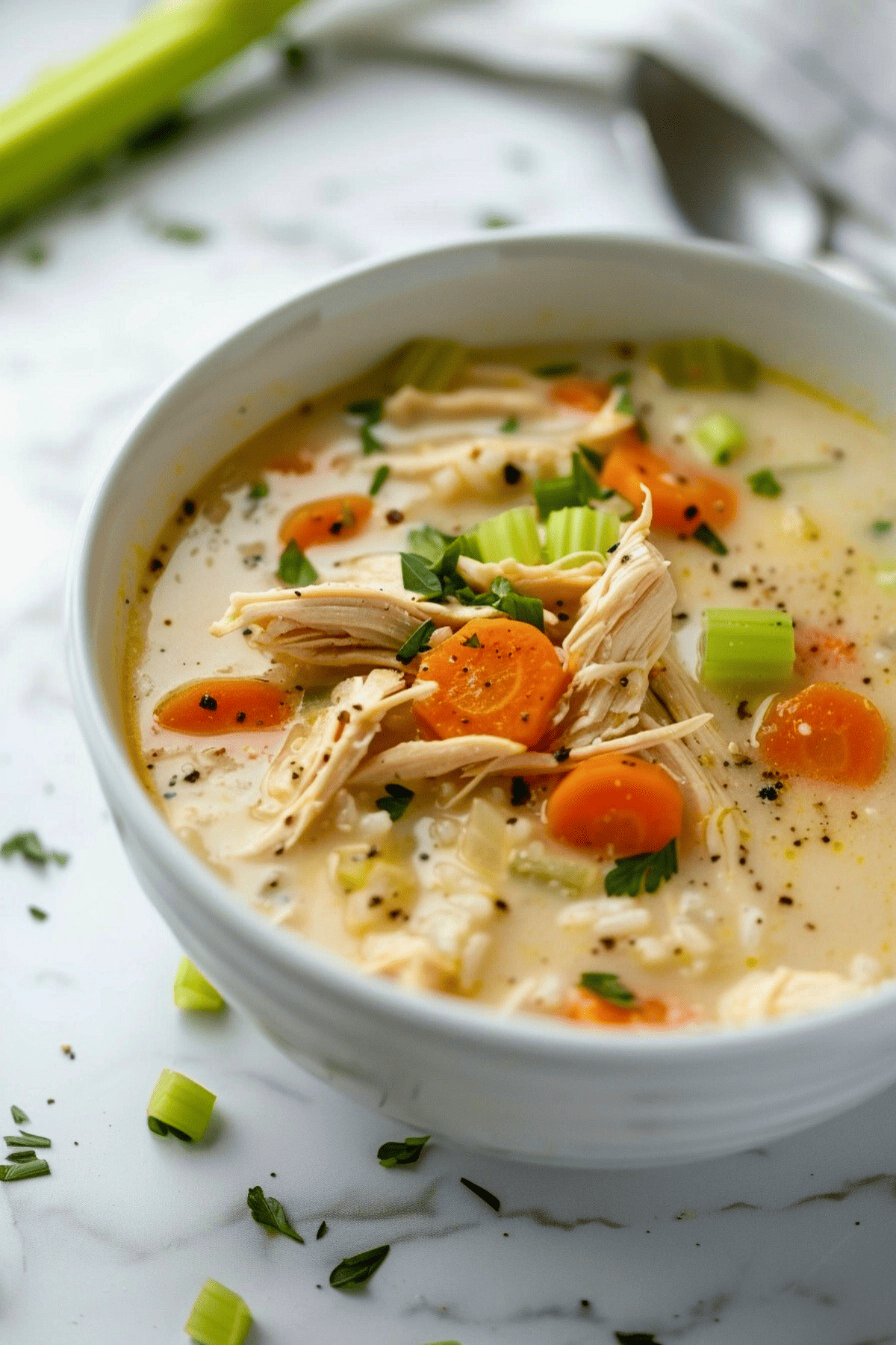 Chicken lemon rice soup served on a white bowl with carrots and celery.