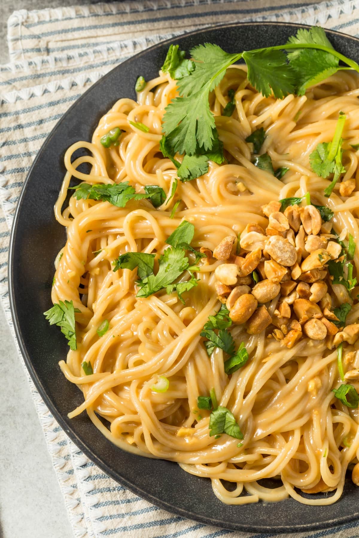 Pasta noodles with creamy peanut sauce and cilantro and peanut garnish served on a black plate.
