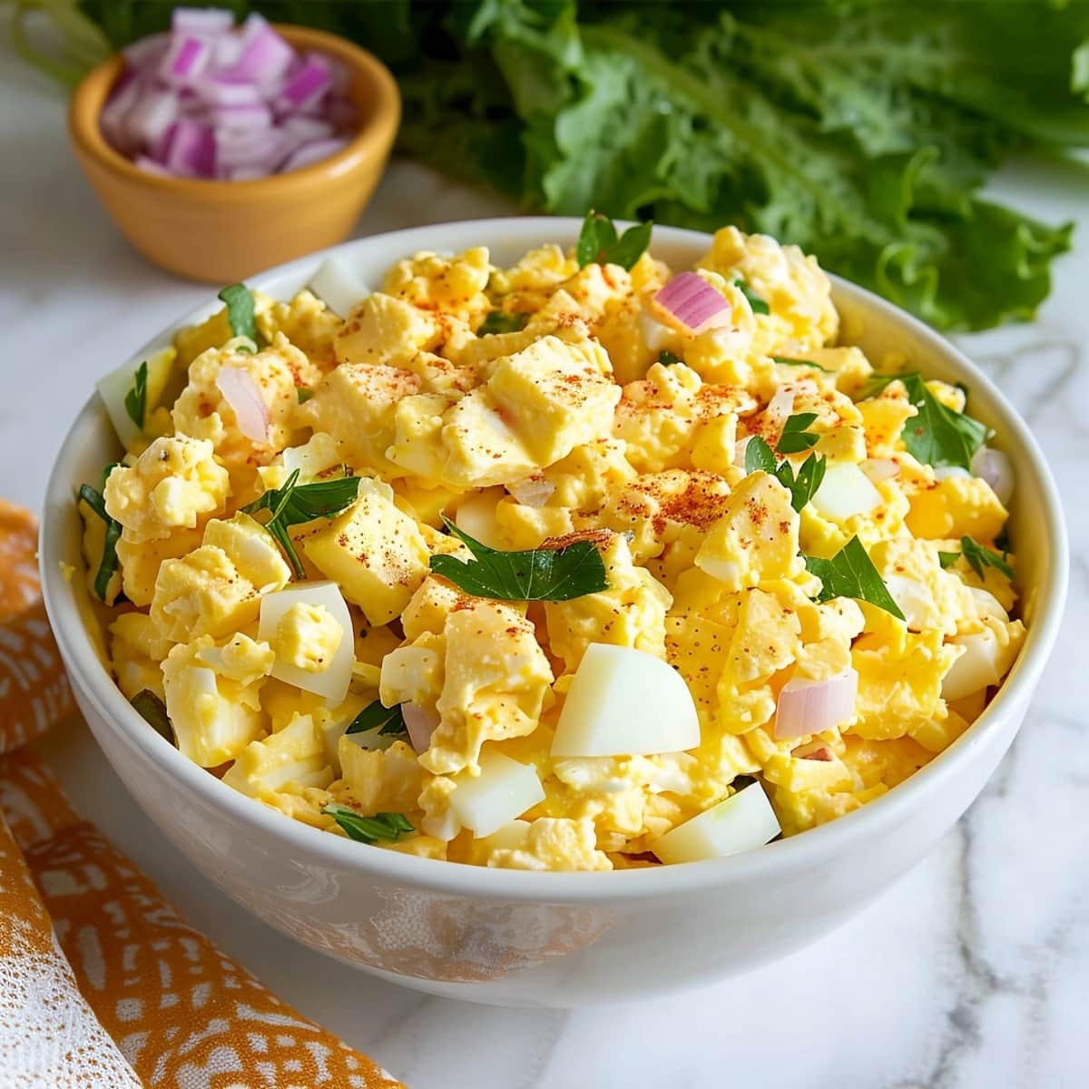 Creamy homemade egg salad in a white bowl on a white marble table