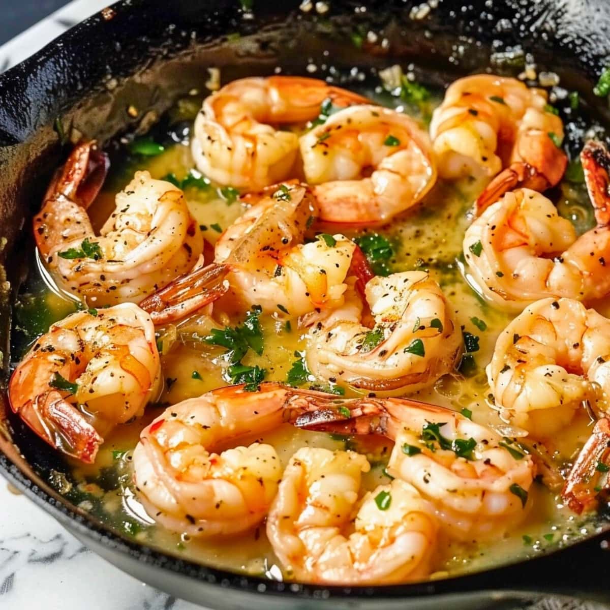 Shrimp in garlic butter sauce cooked in a cast iron pan.