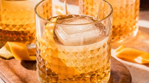 Three glasses of iced Godfather cocktail, featuring orange rinds.