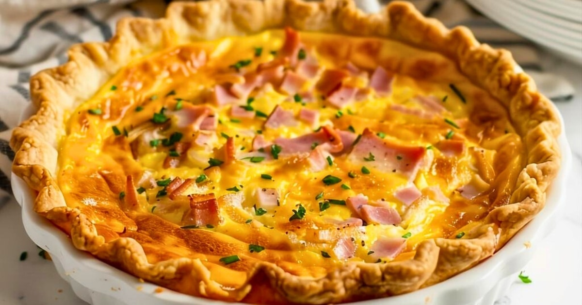 Whole ham and cheese quiche in a white pie dish garnished with chopped parsley.
