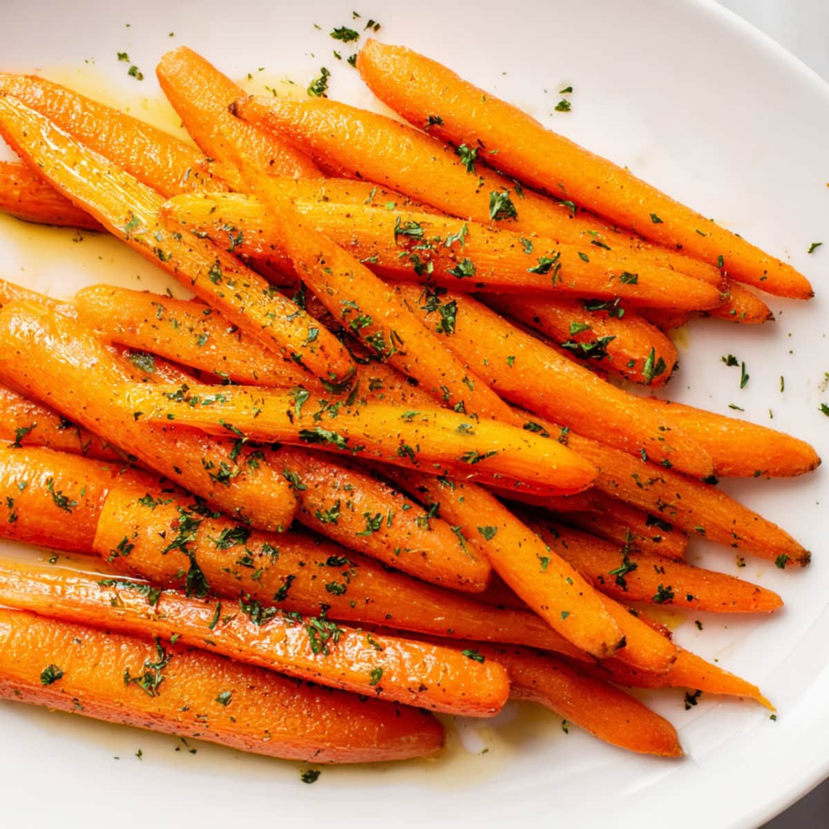 Overhead view of honey roasted carrots with parsley in a white plate.