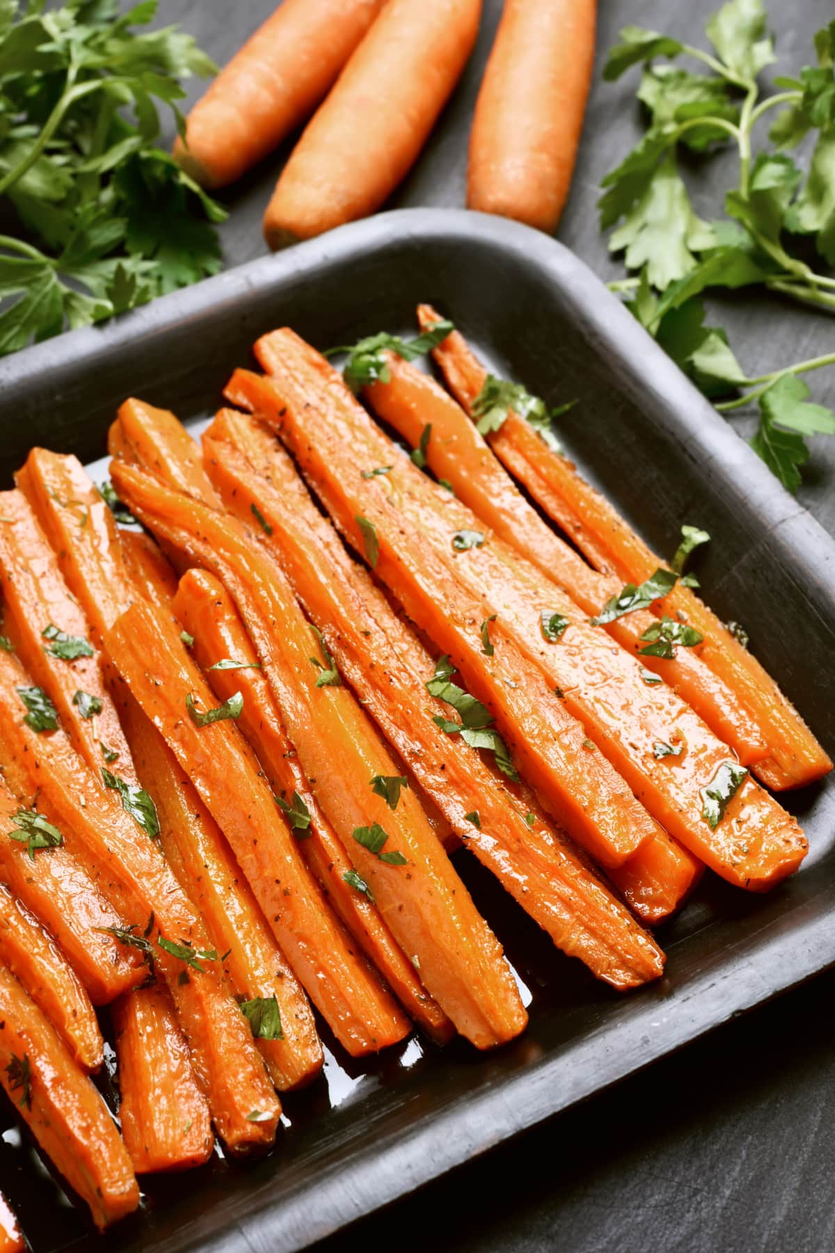 Roasted carrots with honey sprinkled with chopped parsley on a baking dish. 