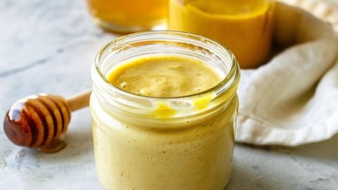 Small glass jar with honey mustard sauce, mustard and honey in jar in the background.