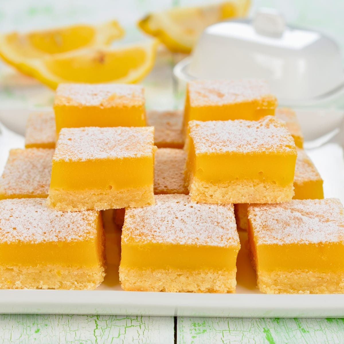 Lemon bars dusted with powdered sugar on top arranged on a plate.
