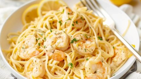 Pasta with shrimp garnished with chopped parsley on a white plate.