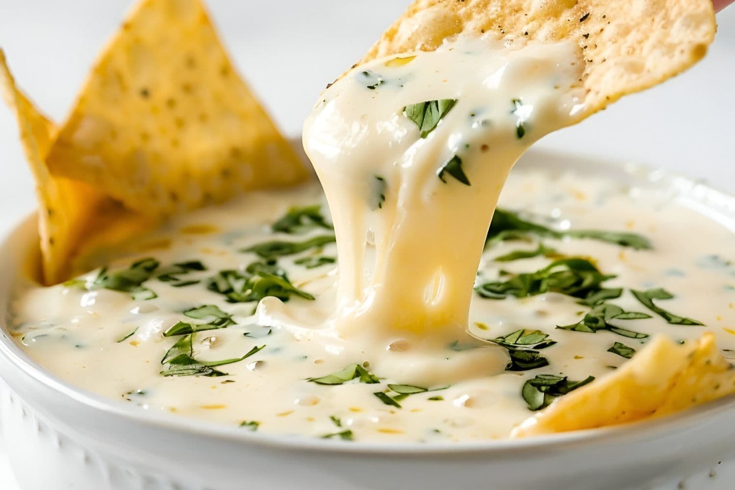Dipping Chip into Mexican White Queso Cheese Dip in a White Bowl with Satisfying Cheese Pull