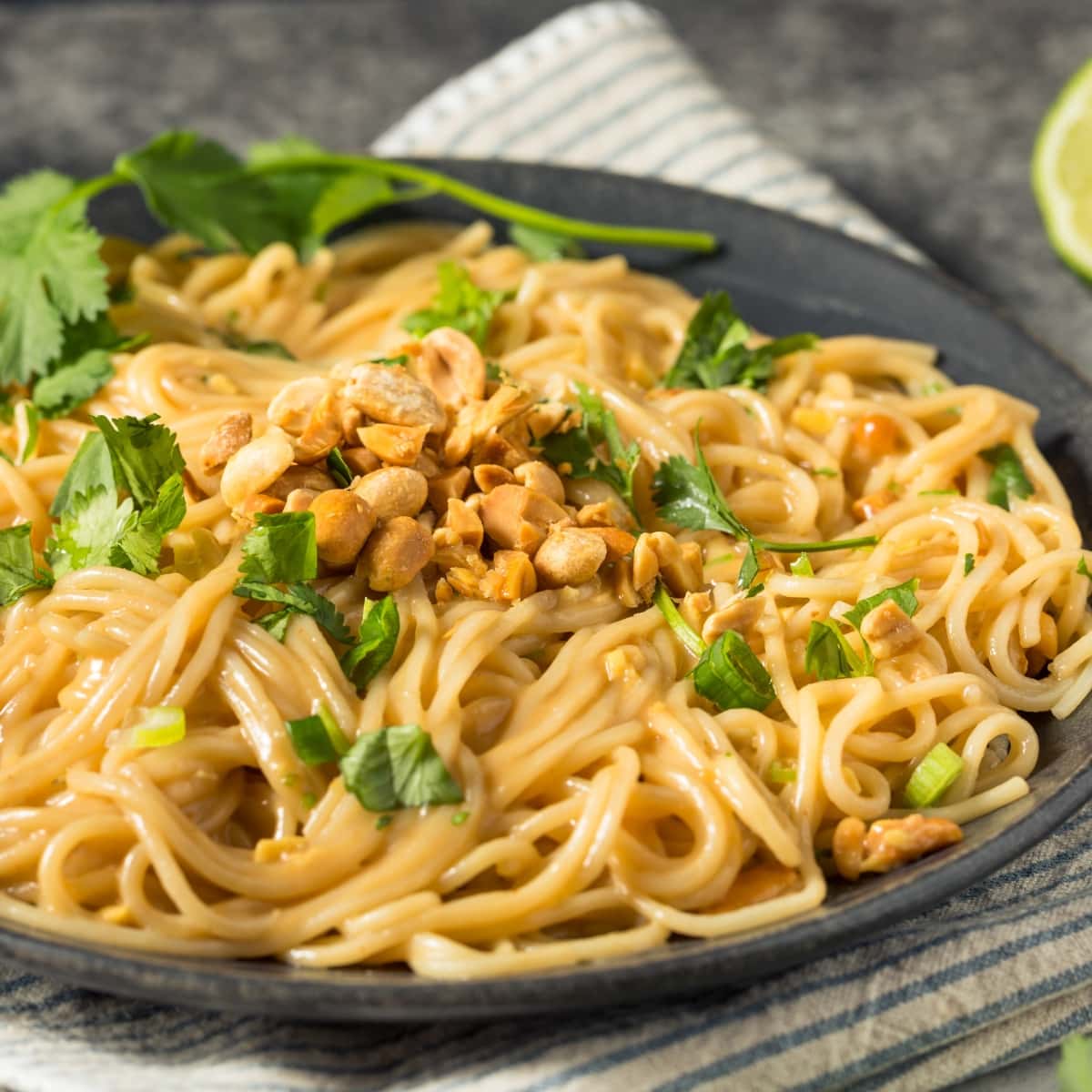 Peanut noodles garnished with fresh cilantro leaves and chopped noodles served on a black plate. 