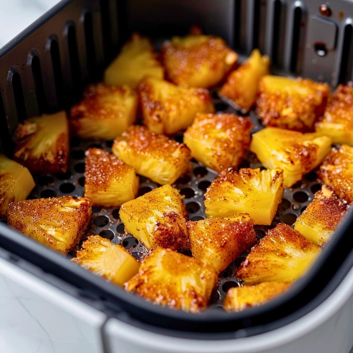 Bite size pineapple coated with cinnamon sugar inside an air fryer.