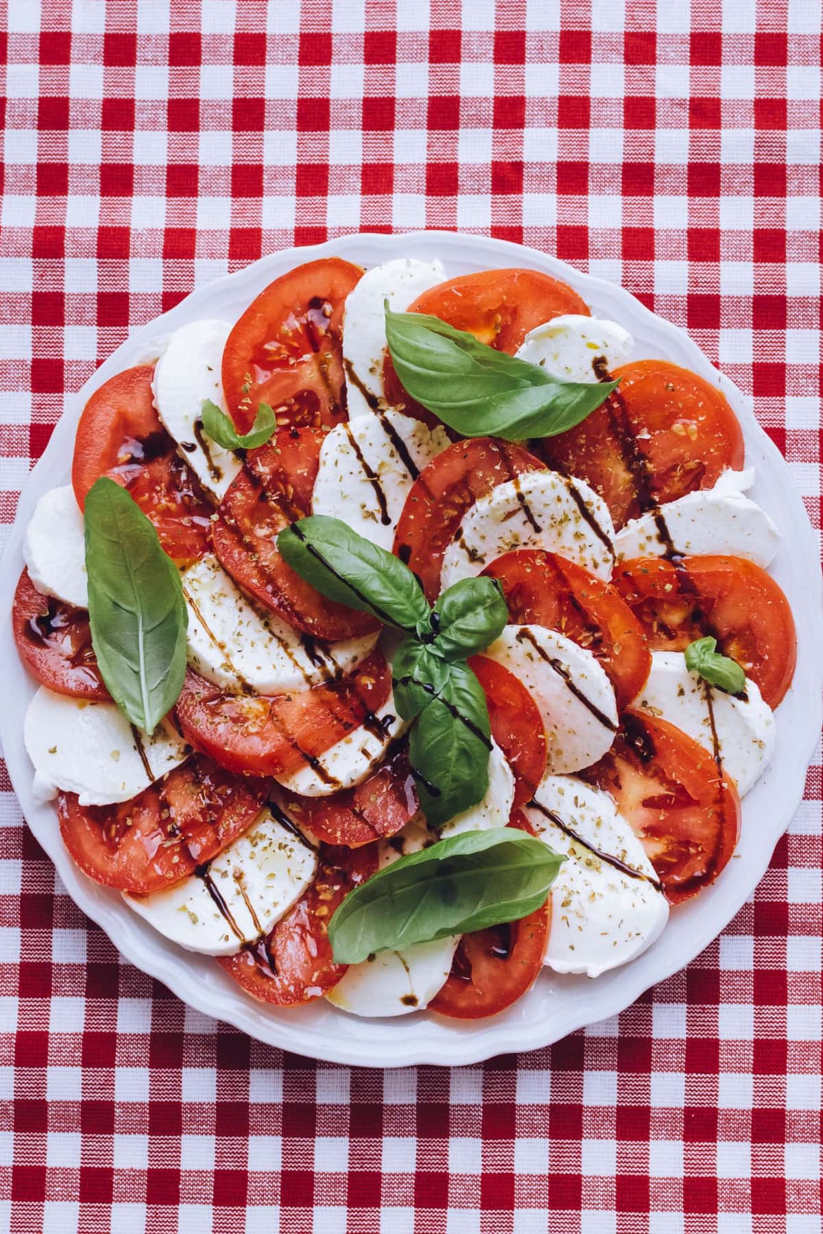 Top view of a platter of Caprese salad made with mozzarella cheese, basil leaves and tomatoes drizzled with balsamic vinegar and olive oil. 