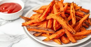 A plateful serving of air fryer sweet potato fries with ketchup on the sides.
