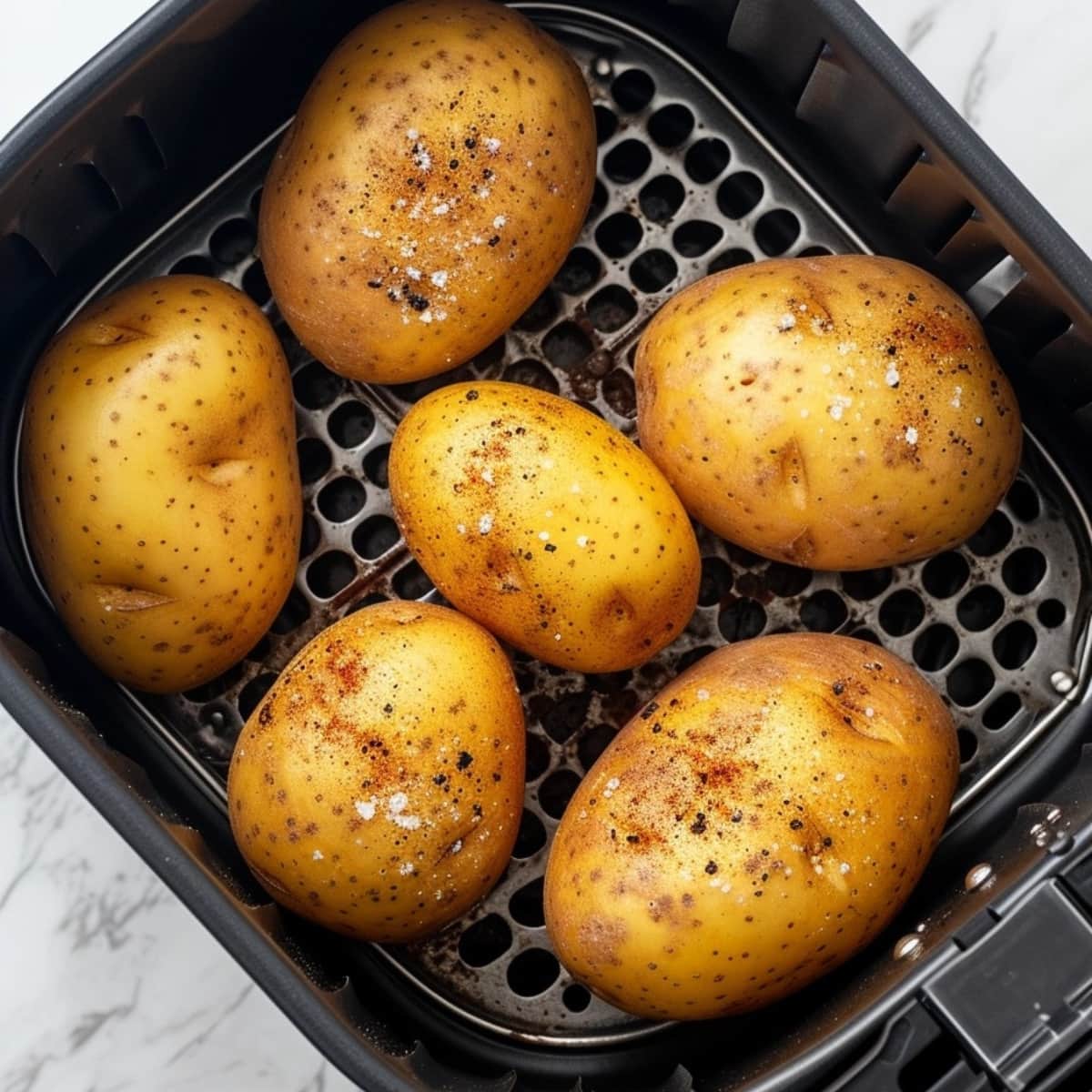 Potatoes seasoned with salt and pepper inside an air fryer basket.
