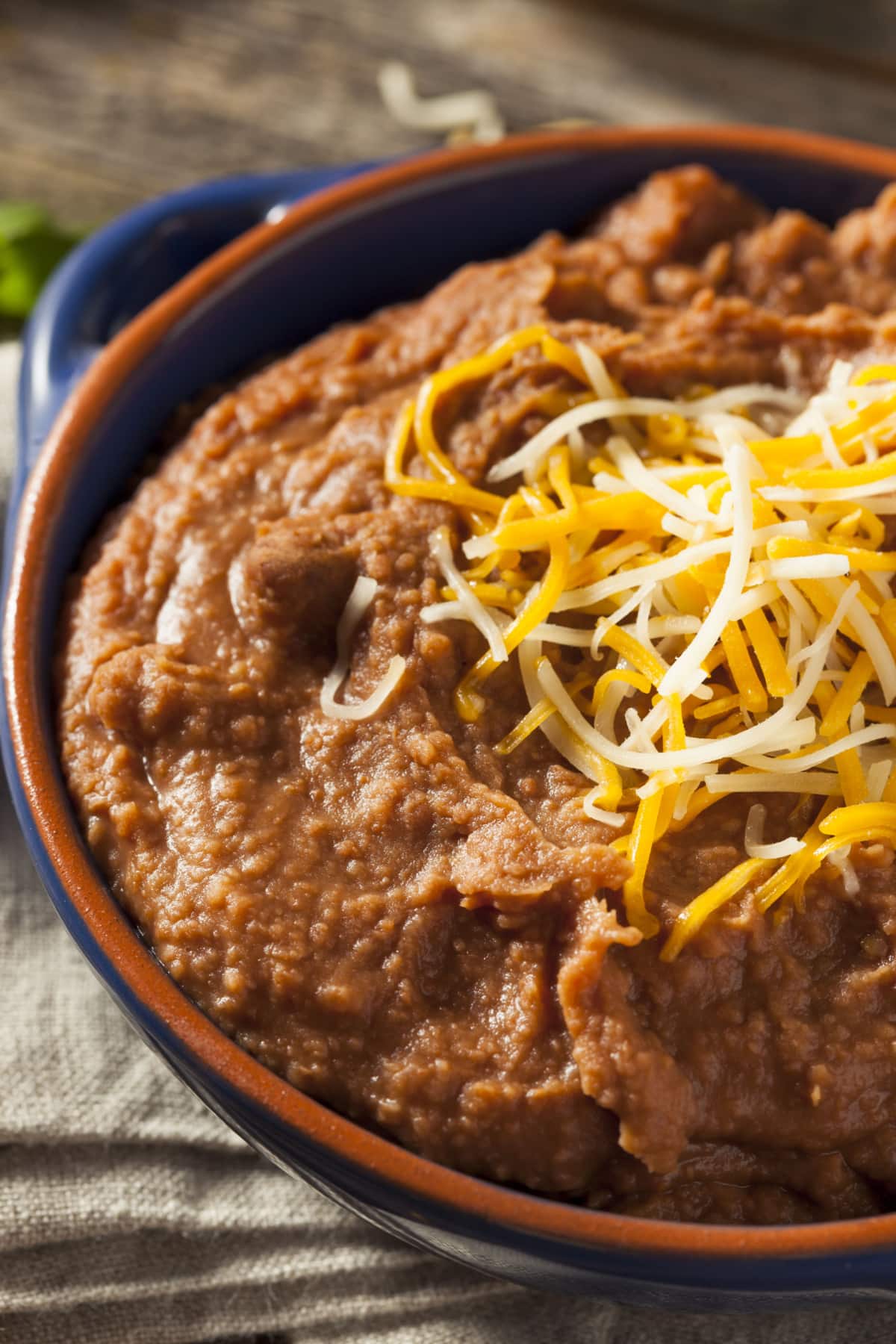 Closeup of creamy refried beans in a blue pot topped with grated cheese. 