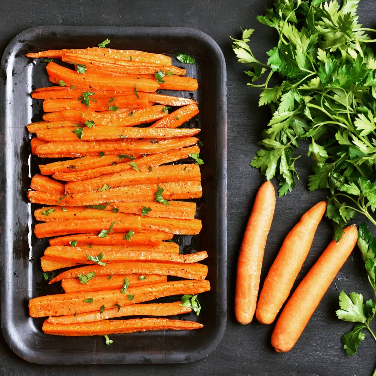 Sliced carrots arranged on a baking pan coated with honey sprinkled with chopped parsley and spices. 