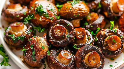 Sauteed garlic butter mushroom on a plate garnished with chopped parsley.