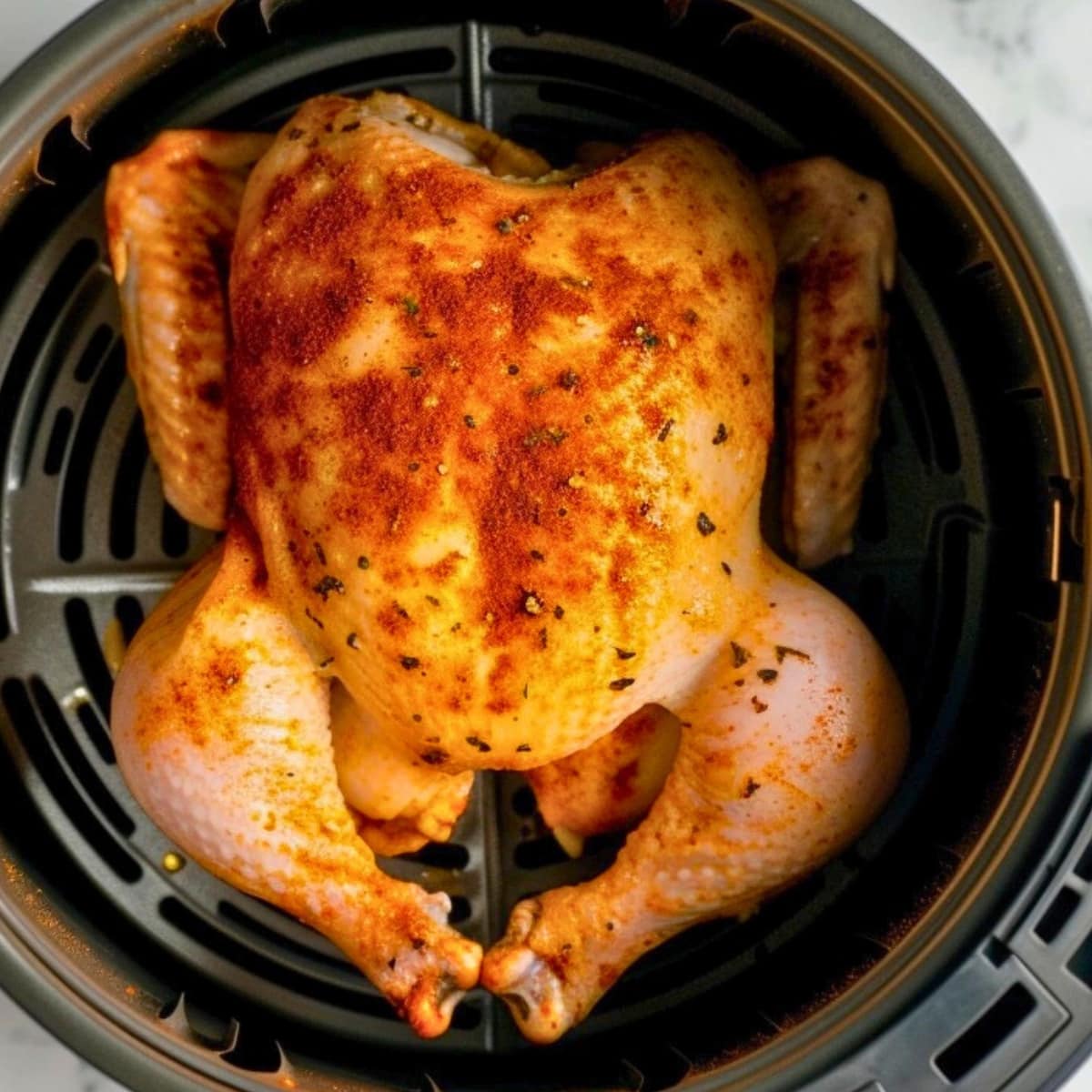 Whole chicken in an air fryer basket covered in spices
