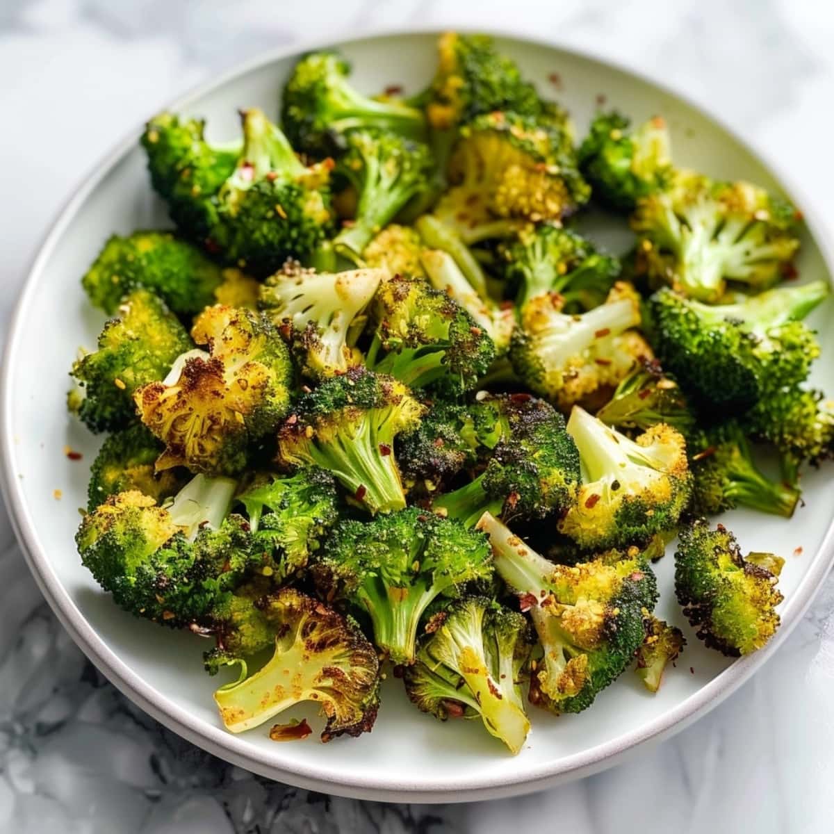 Seasoned air fried broccoli in a white plate on top of white marble table.