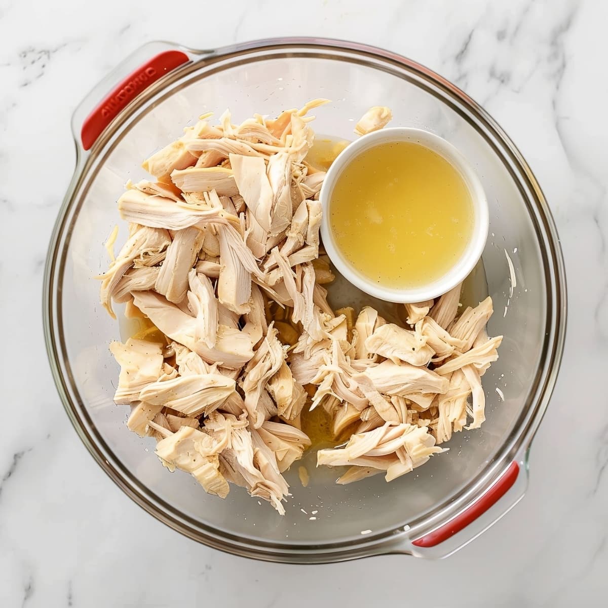 Shredded chicken with chicken broth in a glass bowl, top view