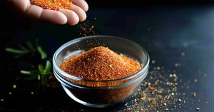 A person sprinkling an old bay seasoning in a small glass container on a dark background