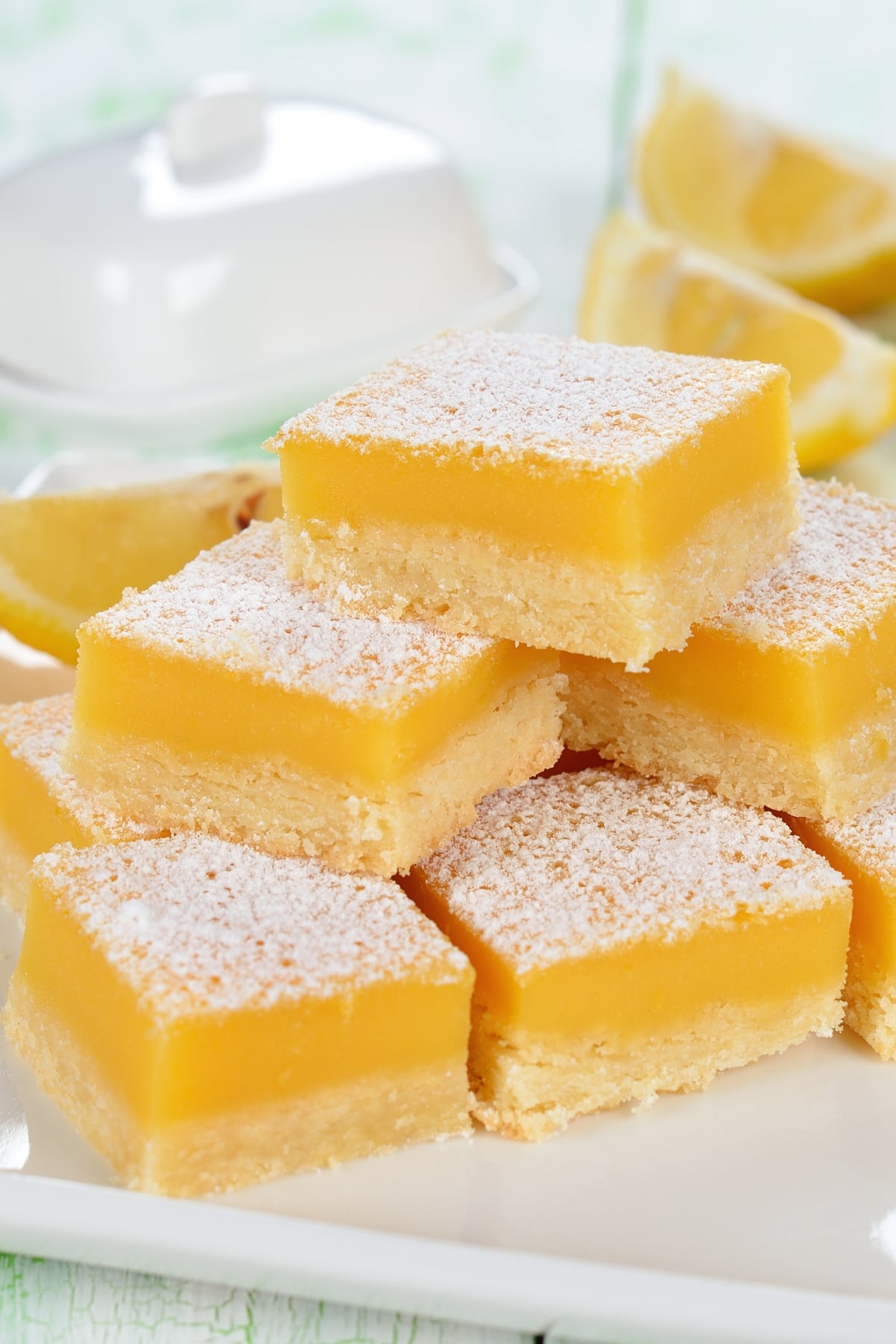 Stack of square cut lemon bars in a plate with powdered sugar toppings.