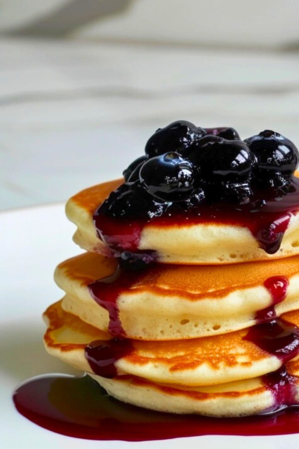 Stack of fluffy pancakes on a plate topped with blueberry jam.