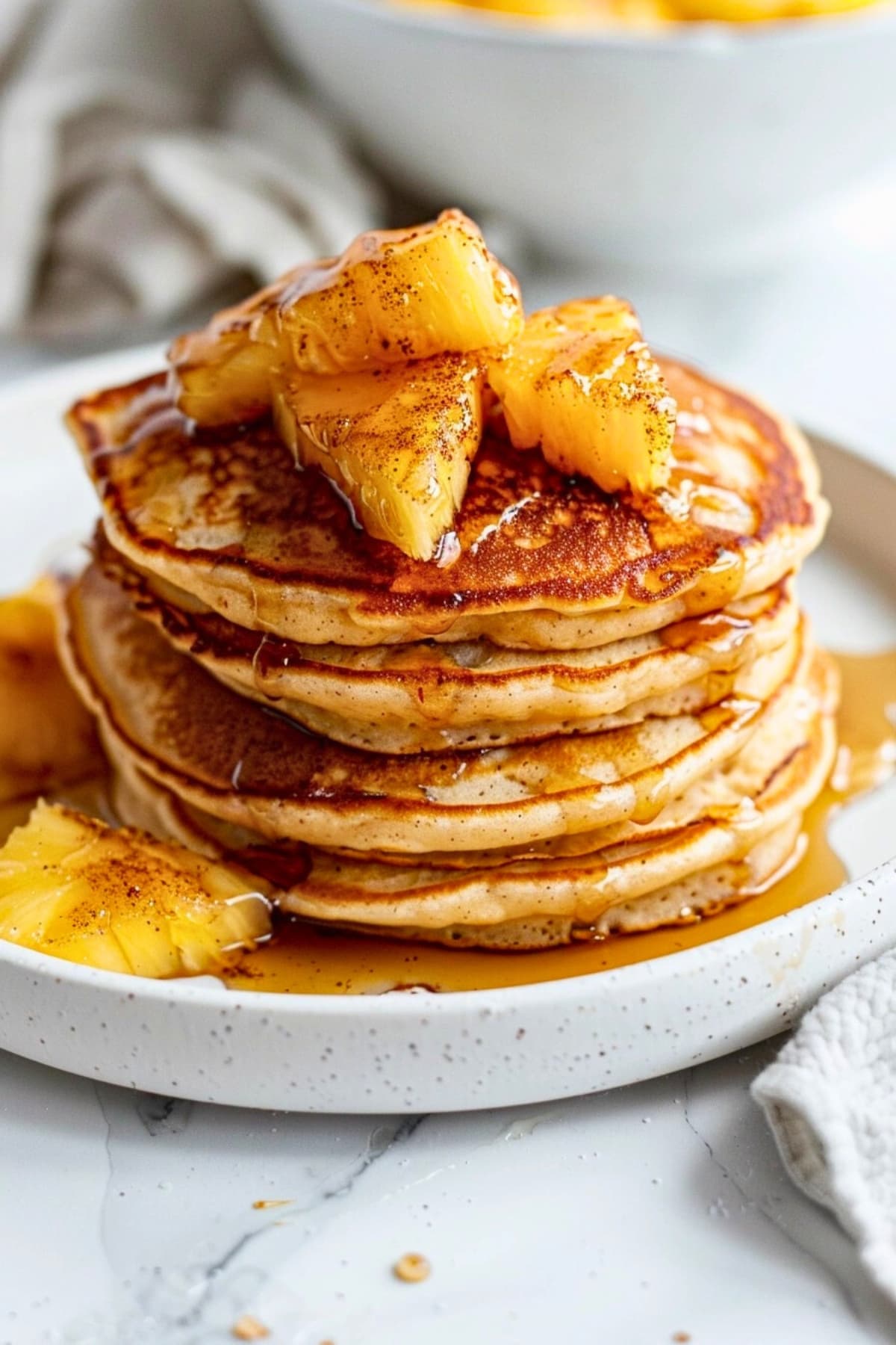 Stack of pancake topped with air fried pineapple bites drizzled with syrup served on a plate.