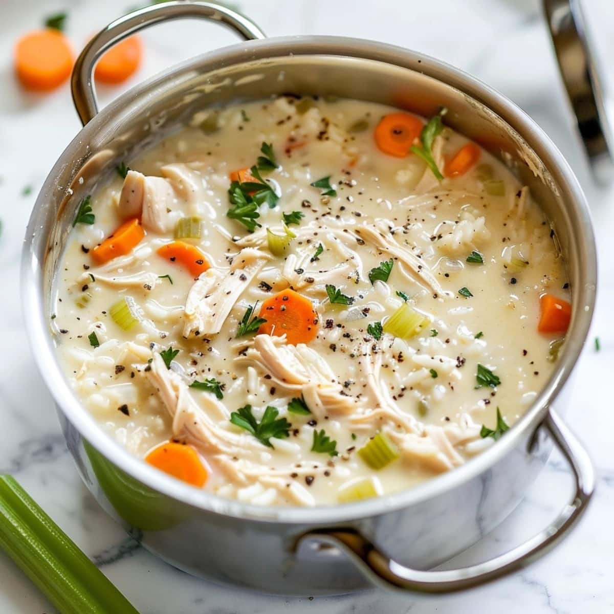 Chicken lemon rice soup in a stainless pot with chopped celery and carrots loaded with shredded chicken.