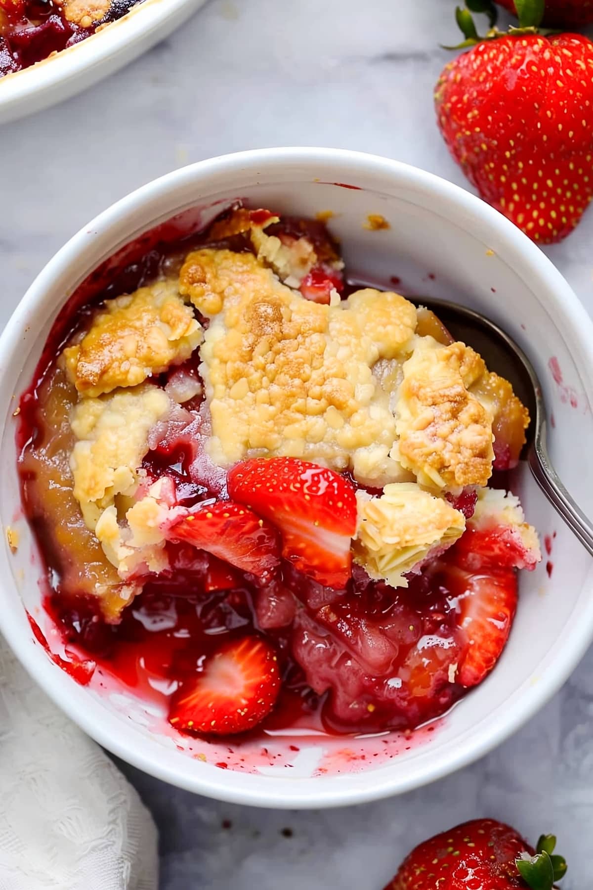 Homemade strawberry cobbler in a white bowl on a white marble table. 