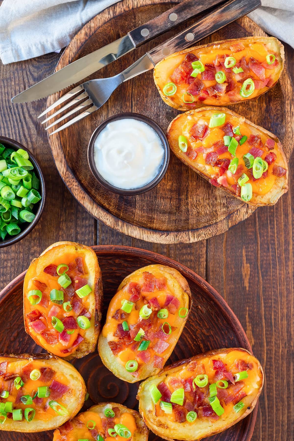 Potato skins with cheesy filling on a wooden tray served with sour cream garnished with bacon and chopped onions.