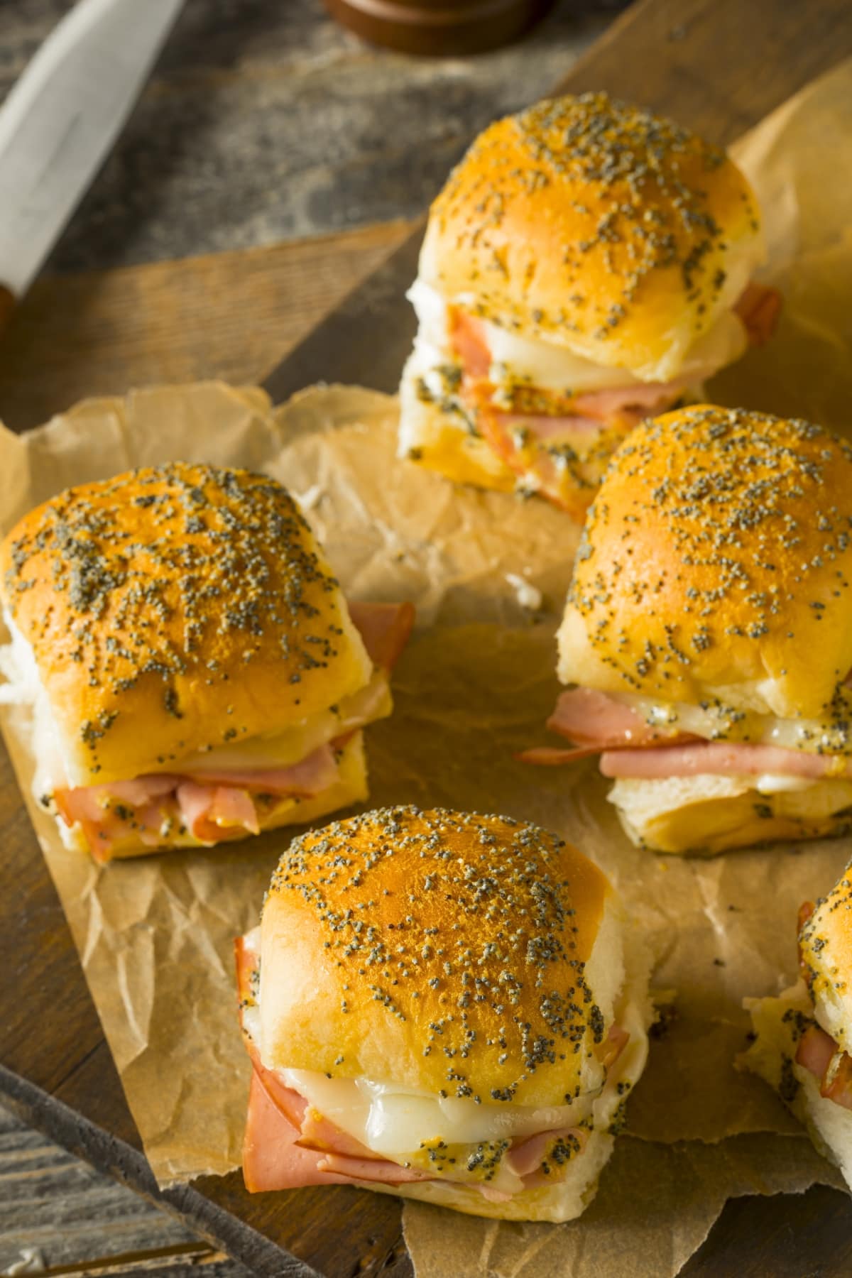 Ham and cheese sliders laid on brown parchment paper.  