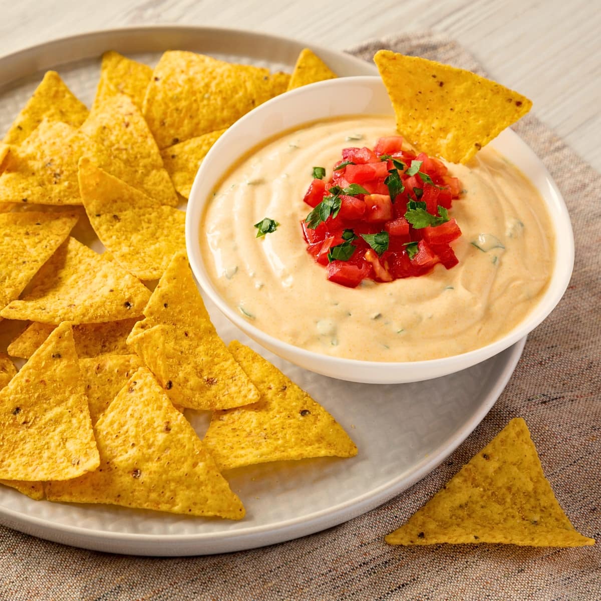 White queso dip in a bowl garnished with salsa served with tortilla chips.