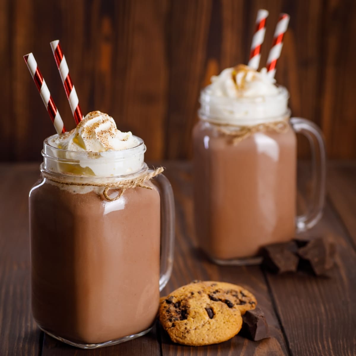 Two glass mugs of chocolate milkshake topped with whipped cream dusted with chocolate