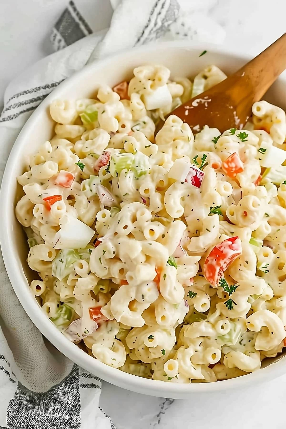 Macaroni salad tossed with a wooden spoon in a white bowl.